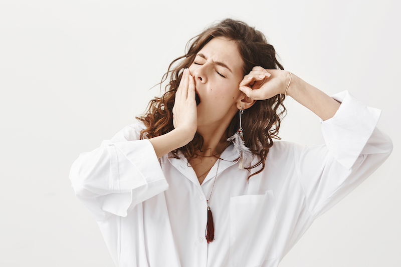 Studio portrait of tired or exhausted young businesswoman yawning and stretching while covering mouth with hand, standing with closed eyes over gray background. this girl has fatigue.