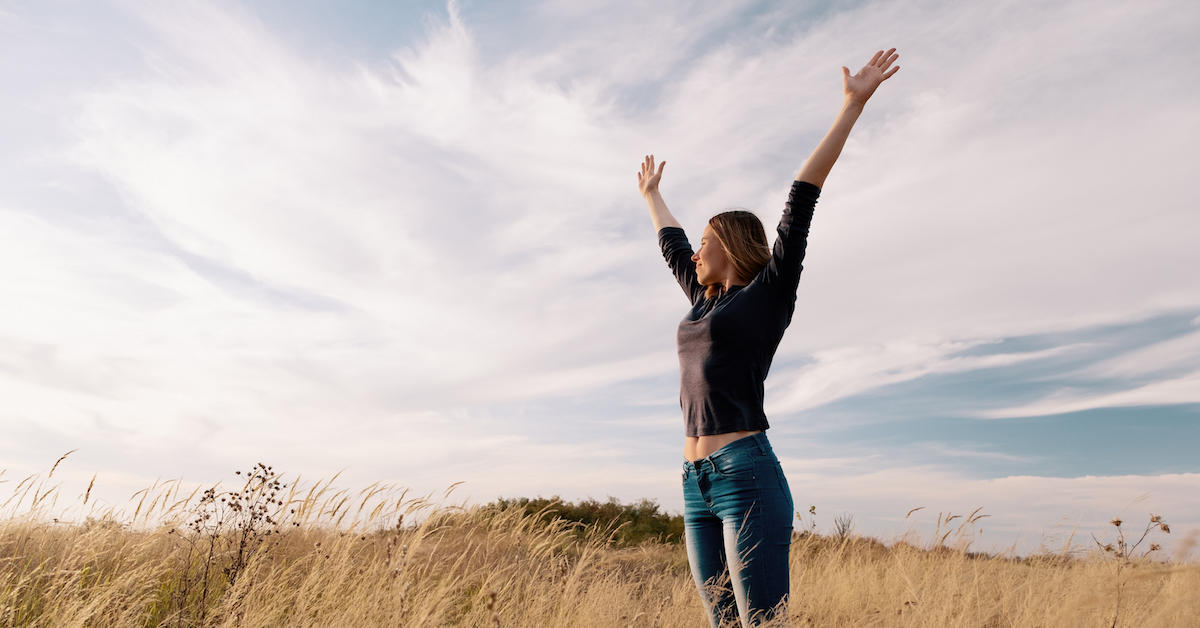 Young happy woman in a golden field on sunset.