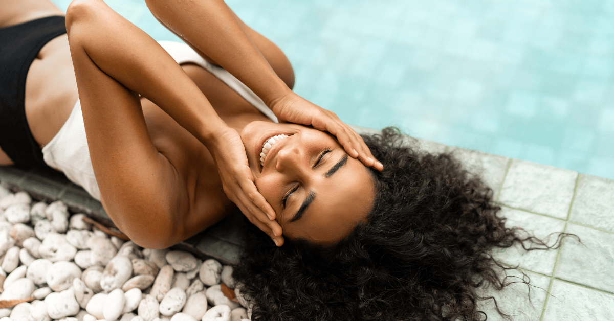 Woman with beautiful curly hair lying beside a pool