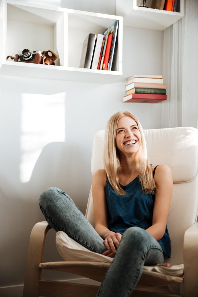 Cheerful beautiful young woman sitting in armchair at home