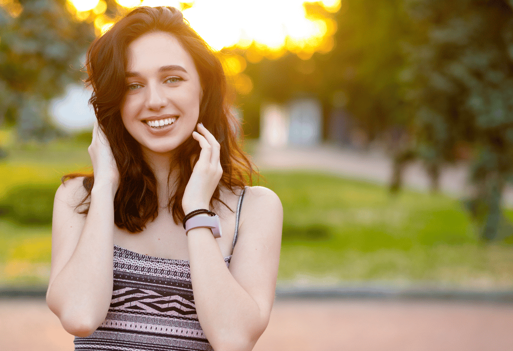 Beautiful smiling woman posing at a park with the sunset on her back