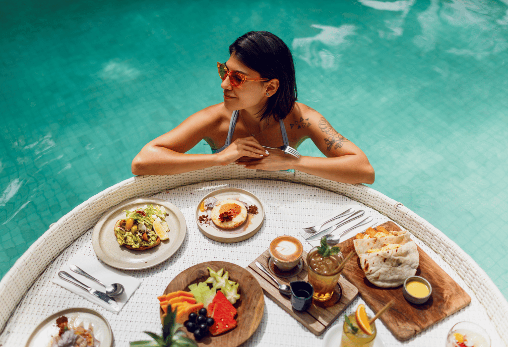 Black-haired woman with tattoos leaning on a tray floating on the pool full of food