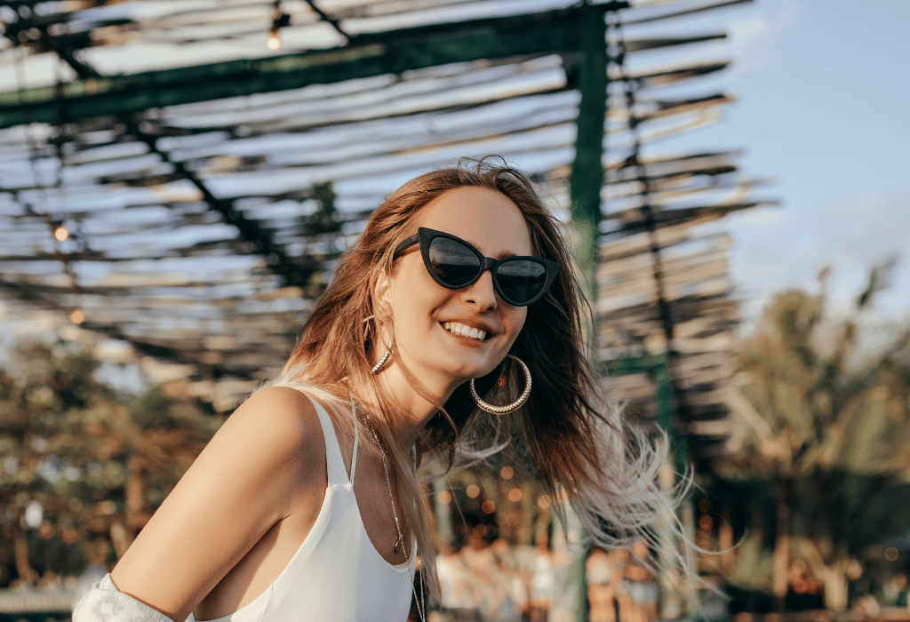 Smiling woman in a white top, black sunglasses and big hoop earrings on a bridge