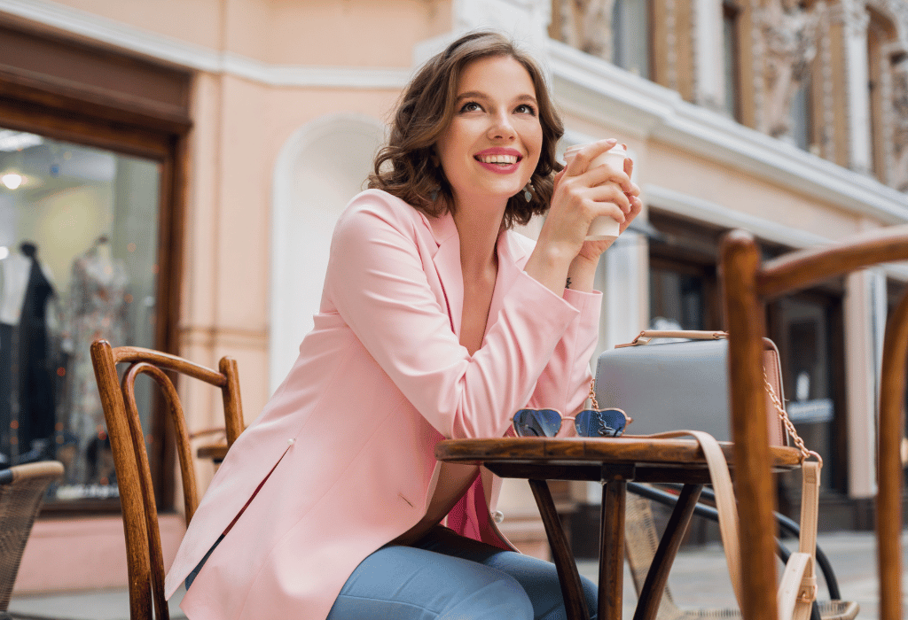 Pretty woman in a pink suit holding a cup of coffee sitting outside a cafe