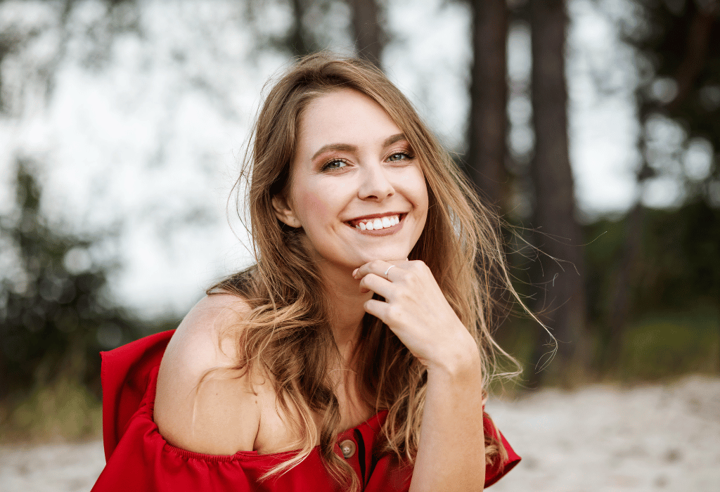 Smiling woman with makeup and wearing a red off-shoulder top