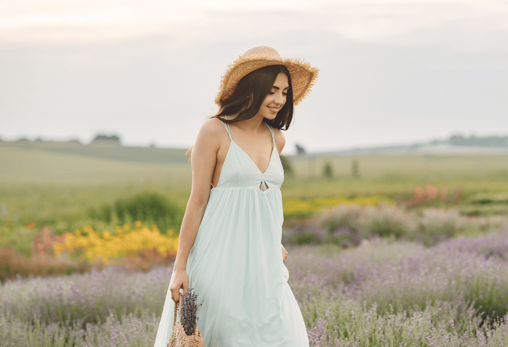 Beautiful woman in a dress and a hat walking in a lavender field with a burlap bag