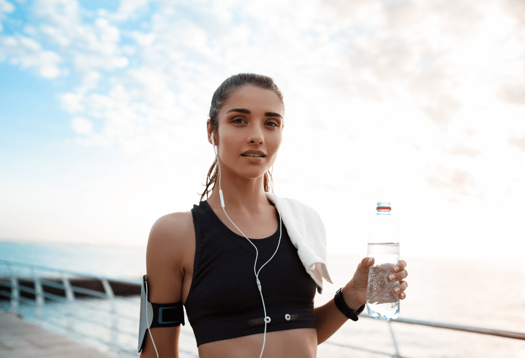 Woman holding a water bottle and wearing earphones on a morning jog